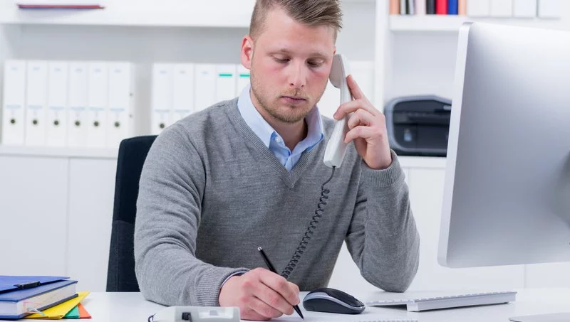 A man is taking notes, while talking on the phone